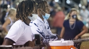 Two masked students watch high school football on sidelines