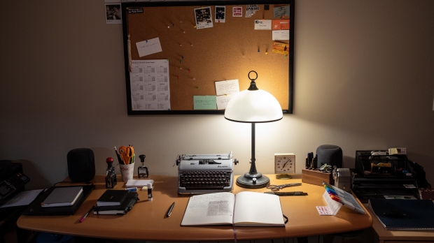 A desk setup with a lit lamp and office supplies on top and a bulletin board on the wall behind.