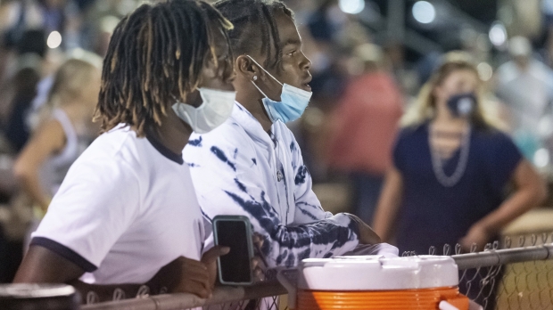 Two masked students watch high school football on sidelines