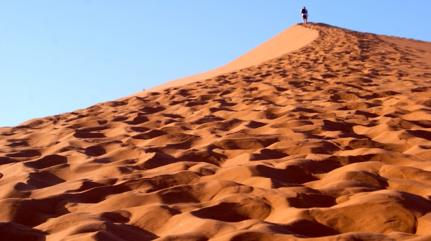 A person walks up a sand dune with footprints behind them