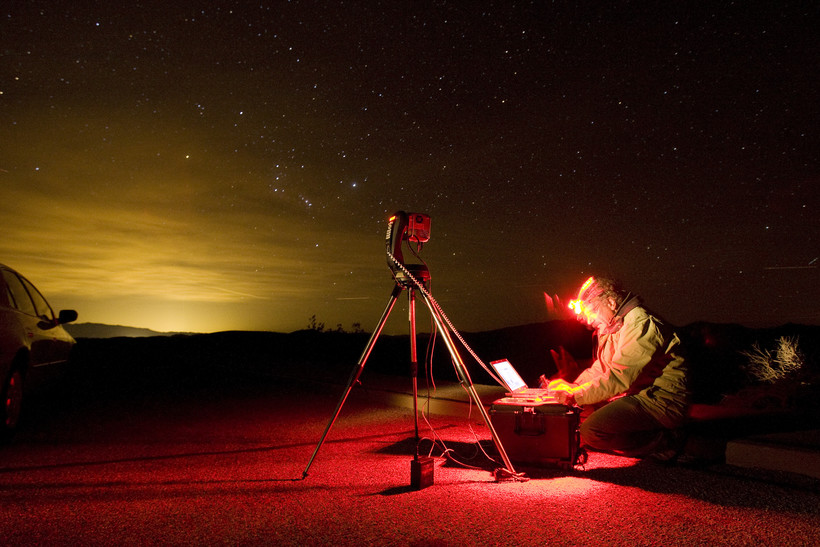 Light glowing in the distance next to a man with a computer in the desert