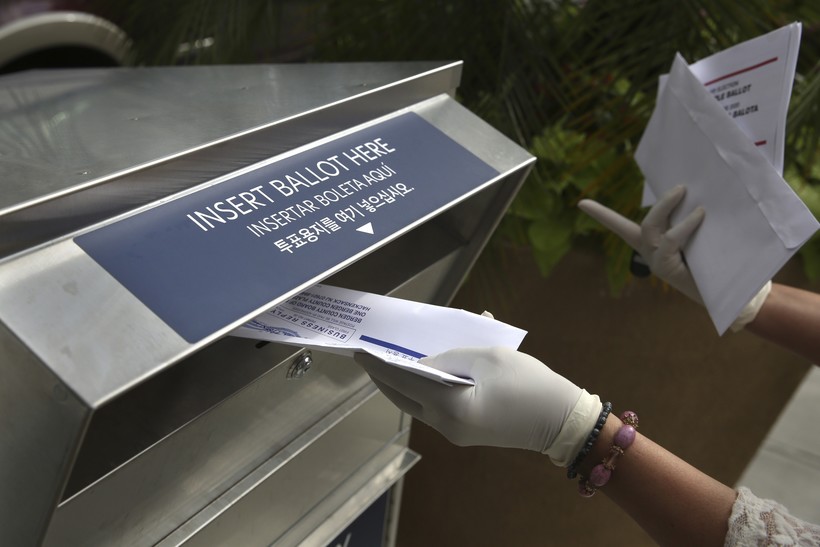 A woman drops off a mail-in ballot at a drop box 