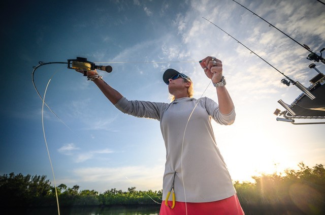 Jen holds a reel  with the sun and tree line behind her. 